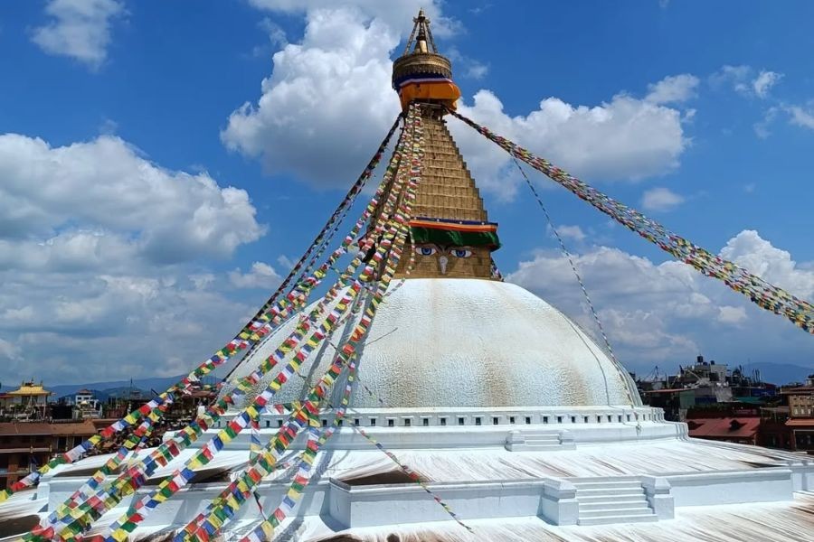 Boudhanath Stupa with colorful prayer flags under blue sky.
